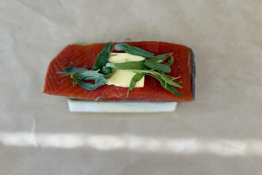  Then, place the salmon fillet (skin side down) on top of the herbs and top it with a slice of butter and more herbs. 