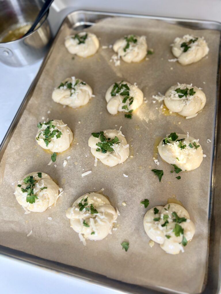 Liberally brush the garlic butter over each garlic knot and sprinkle the cheese and parsley on top. If you have any garlic butter left over you can save for brushing after they bake.