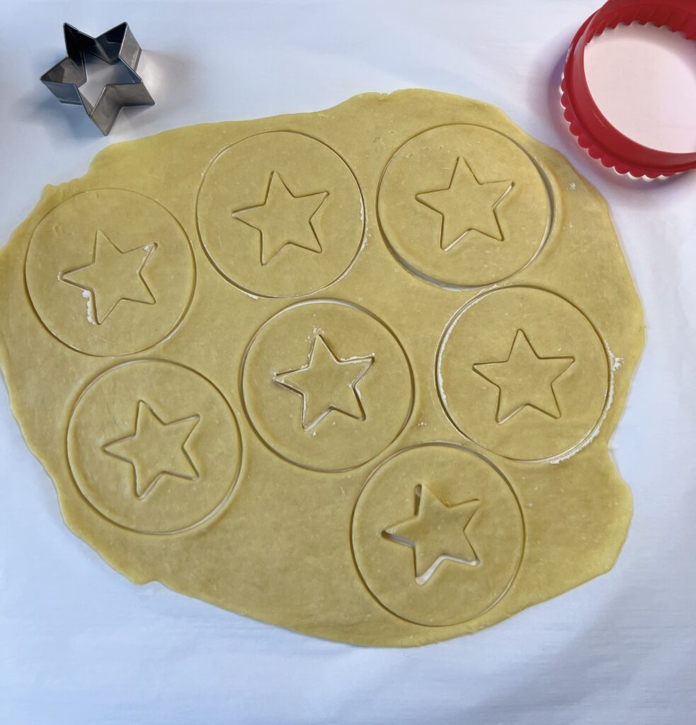 Cut the cookies into desired shapes and place them onto the baking sheet. I use a 3-inch round cookie cutter and cut out a star in the middle of each. Make sure to create a top and bottom for each cookie. 