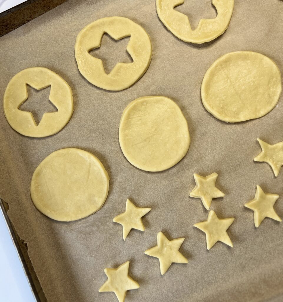 Cut the cookies into desired shapes and place them onto the baking sheet. I use a 3-inch round cookie cutter and cut out a star in the middle of each. Make sure to create a top and bottom for each cookie. 